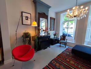 A room with a red chair, a chandelier, a patterned rug, and a window with a view. - Large, luxurious family home in Haarlem, close to city, beach and Amsterdam. (Haarlem)