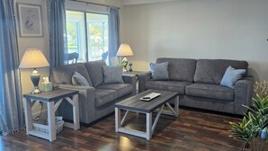 Ein Wohnzimmer mit zwei grauen Sofas, einem Couchtisch und einem Beistelltisch mit Lampen.