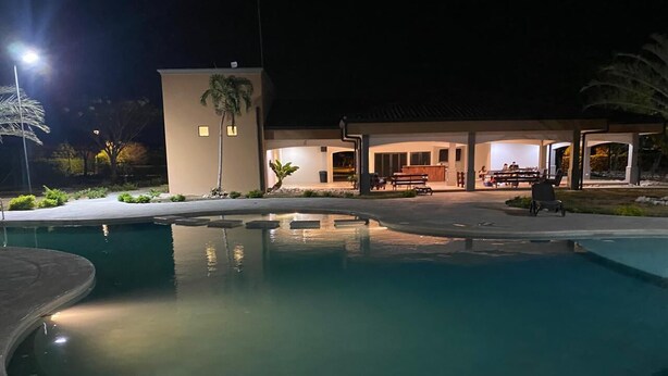 A swimming pool with a curved edge, a covered outdoor seating area, and a building with a flat roof in the background. - Equipped house in Liberia for long stays (Liberia)