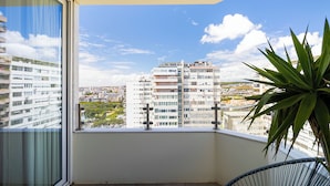 Un balcon avec vue sur des immeubles de grande hauteur, un pot de fleurs et une chaise.