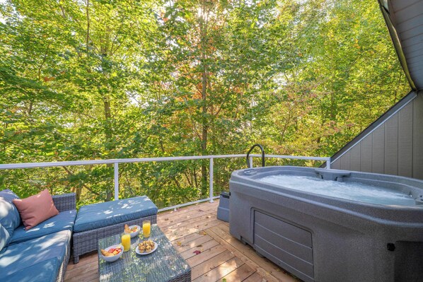 Eine Terrasse mit Whirlpool, Sitzgelegenheit und Blick auf einen Wald.