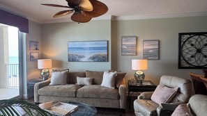 Ein Wohnzimmer mit einer Couch, Sesseln, einem Couchtisch und einem Deckenventilator. An den Wänden sind Lampen und Kunstwerke angebracht.