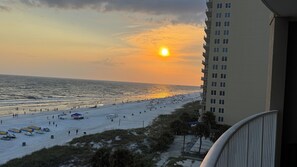 A beach with a sunset, a pier in the distance, and a building with balconies. - Cozy beach Front , great location unit 601 (Panama City Beach)