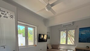 Ein Schlafzimmer mit Bett, Deckenventilator, Fernseher und Fenstern.