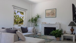 Ein Wohnzimmer mit einer Couch, einem Kamin, einem Fernseher und einem Fenster mit Blick auf Bäume.