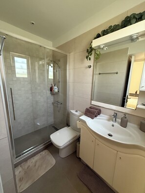 Et moderne badeværelse med en glasafskærmet bruseniche, et hvidt toilet, en vask med spejl og en håndklæderække.