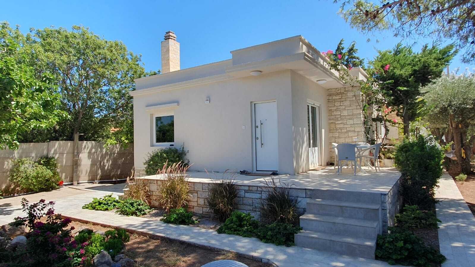 Une maison moderne avec une façade en pierre, un petit porche et un jardin agrémenté de diverses plantes.