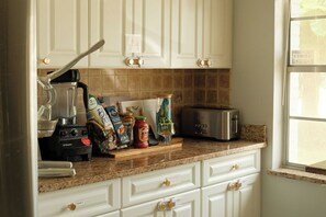 A kitchen with white cabinets, a granite countertop, a blender, a toaster, and various food items. - Casa Sol Boho chic pool home, sun soaked & spacious, king bed fireplace sleeps 8 (Fort Pierce)
