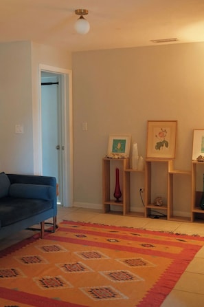 Ein Wohnzimmer mit einem blauen Sofa, einem gemusterten Teppich und Holzböden mit Dekoartikeln.