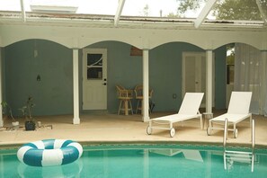 Un espace extérieur avec piscine, des chaises longues, un patio couvert et une porte donnant accès à un espace intérieur.