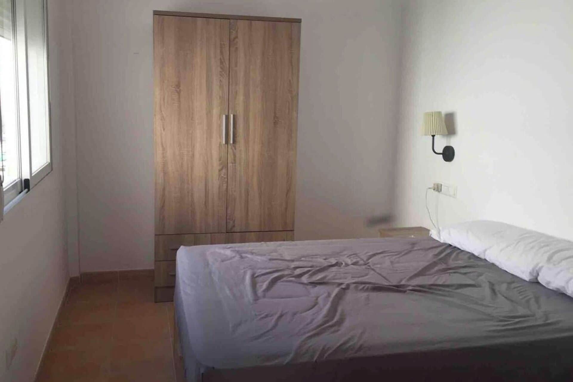 Ein Schlafzimmer mit einem Bett, einem Kleiderschrank, einer Wandlampe und einem Fenster.