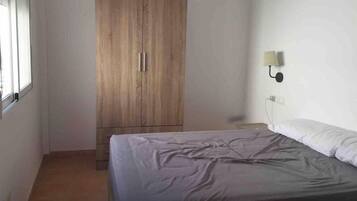 Ein Schlafzimmer mit einem Bett, einem Kleiderschrank, einer Wandlampe und einem Fenster.