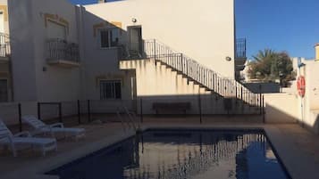 Zwembad met een trap naar een balkon, omgeven door een gebouw met meerdere ramen en een bank.