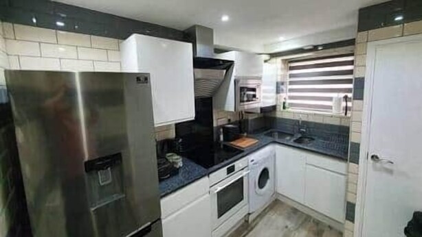 Cozinha compacta com geladeira de aço inoxidável, forno embutido, máquina de lavar e um pequeno balcão.