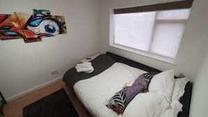 Quarto com cama, janela e parede com uma obra de arte colorida.