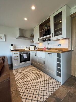 A compact kitchen with white cabinets, a built-in oven, a coffee maker, and a patterned rug. - The Snug, Beautiful luxury 1 Bed Ground floor Cottage with outstanding views... (Cragg Vale)
