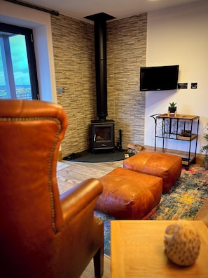 A living room with a fireplace, leather furniture, a TV, and a patterned rug. - The Snug, Beautiful luxury 1 Bed Ground floor Cottage with outstanding views... (Cragg Vale)