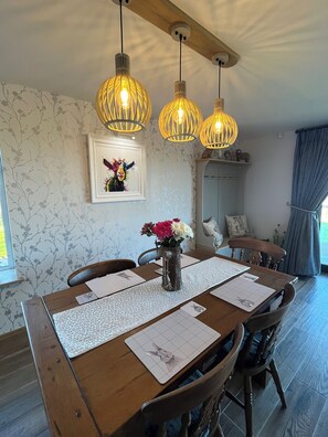 A dining area with a wooden table, chairs, a vase with flowers, and hanging pendant lights. - The Snug, Beautiful luxury 1 Bed Ground floor Cottage with outstanding views... (Cragg Vale)