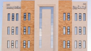 Un moderno edificio de hotel con entrada central, varias ventanas y un cartel que indica que es el hotel Rawaq Suites.