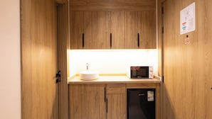 Una kitchenette compacta con armarios de madera, un lavamanos blanco, un microondas y un refrigerador negro.