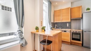 A modern kitchen with wooden cabinets, a stainless steel refrigerator, a built-in oven, and a small bar area with a stool. - Lively City Getaway for 10 Near Meir (Antwerp)