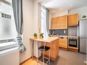 A modern kitchen with wooden cabinets, a stainless steel refrigerator, a built-in oven, and a small bar area with a stool. - Lively City Getaway for 10 Near Meir (Antwerp)