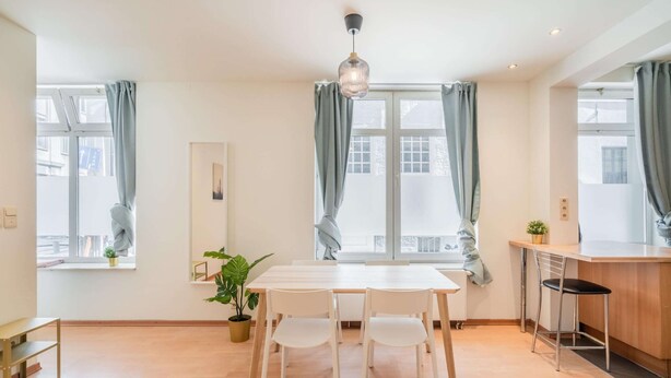 A modern kitchen with a dining table and chairs, a hanging light fixture, and a window with curtains. - Lively City Getaway for 10 Near Meir (Antwerp)