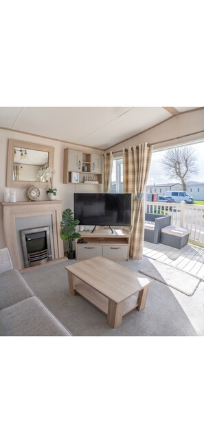 Ein gemütliches Wohnzimmer mit Kamin, Fernseher und bequemen Sitzgelegenheiten.