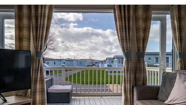 A room with a TV, a sofa, and a window with curtains. - A luxury Caravan in a suburb location. 
       AJH Holiday Homes, Ty Mawr. (Towyn)