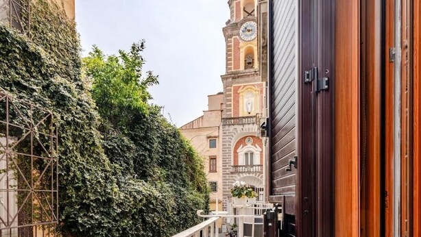 Un estrecho callejón con un edificio cubierto de hiedra en un lado y una torre del reloj al fondo.