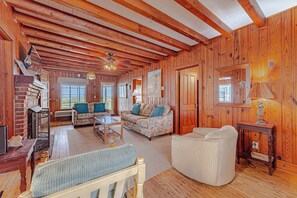 L’intérieur chaleureux d’un chalet avec des murs en bois, une cheminée, deux canapés, une table basse et un ventilateur de plafond.