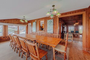 Ein großer Holzesstisch mit Stühlen, eine Küchenzeile und ein Wohnzimmer mit einer Couch und Sesseln.