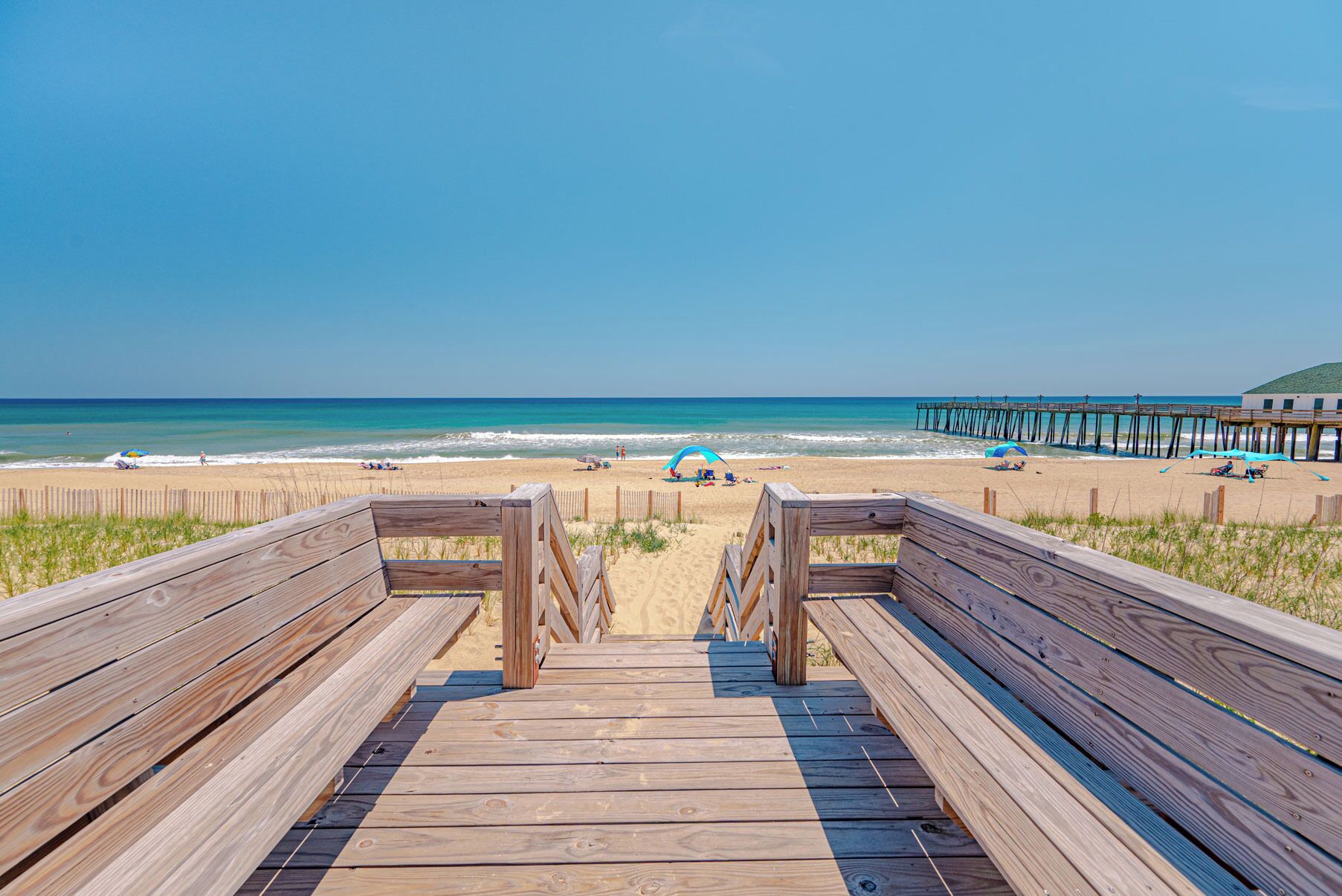Una passerella in legno che conduce a una spiaggia, con un molo sullo sfondo.