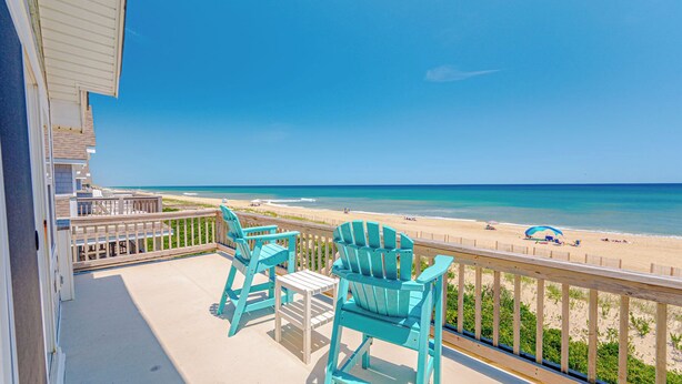 Ein Balkon mit zwei Stühlen und einem Tisch, mit Blick auf einen Strand und einer Holzbrüstung.