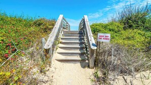 Eine Holztreppe führt zu einem Strand, an dem ein Schild mit der Aufschrift 'KEEP OFF THE DUNES' steht.