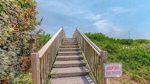 Una escalera de madera con un letrero que dice 'KEEP OFF THE DUNES', rodeada de follaje.