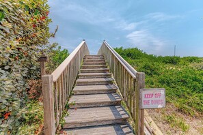 Eine Holztreppe mit einem Schild mit der Aufschrift 'KEEP OFF THE DUNES', umgeben von Grünpflanzen.