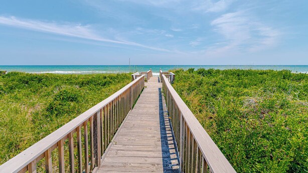 Un paseo marítimo de madera que conduce a la playa, rodeado de vegetación.