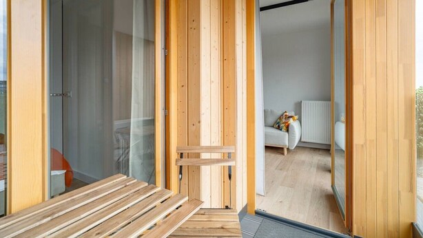 Un interior de madera con un banco, un ventanal corredero y un sofá blanco al fondo.