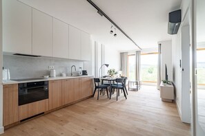 A modern kitchen with wooden cabinets, a built-in oven, and a dining area with a table and chairs. - Portowa M1 - Vistula River nearby, Parking, Balcony - by Rentujemy (Kraków)