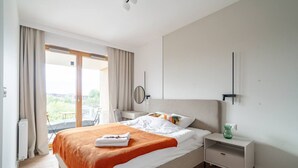 Habitación de hotel con cama, mesita de noche, una silla, ventana con cortinas y vistas al exterior con vegetación.