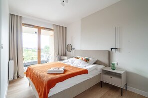 A hotel room with a bed, a bedside table, a chair, a window with curtains, and a view of greenery outside. - Portowa M1 - Vistula River nearby, Parking, Balcony - by Rentujemy (Kraków)