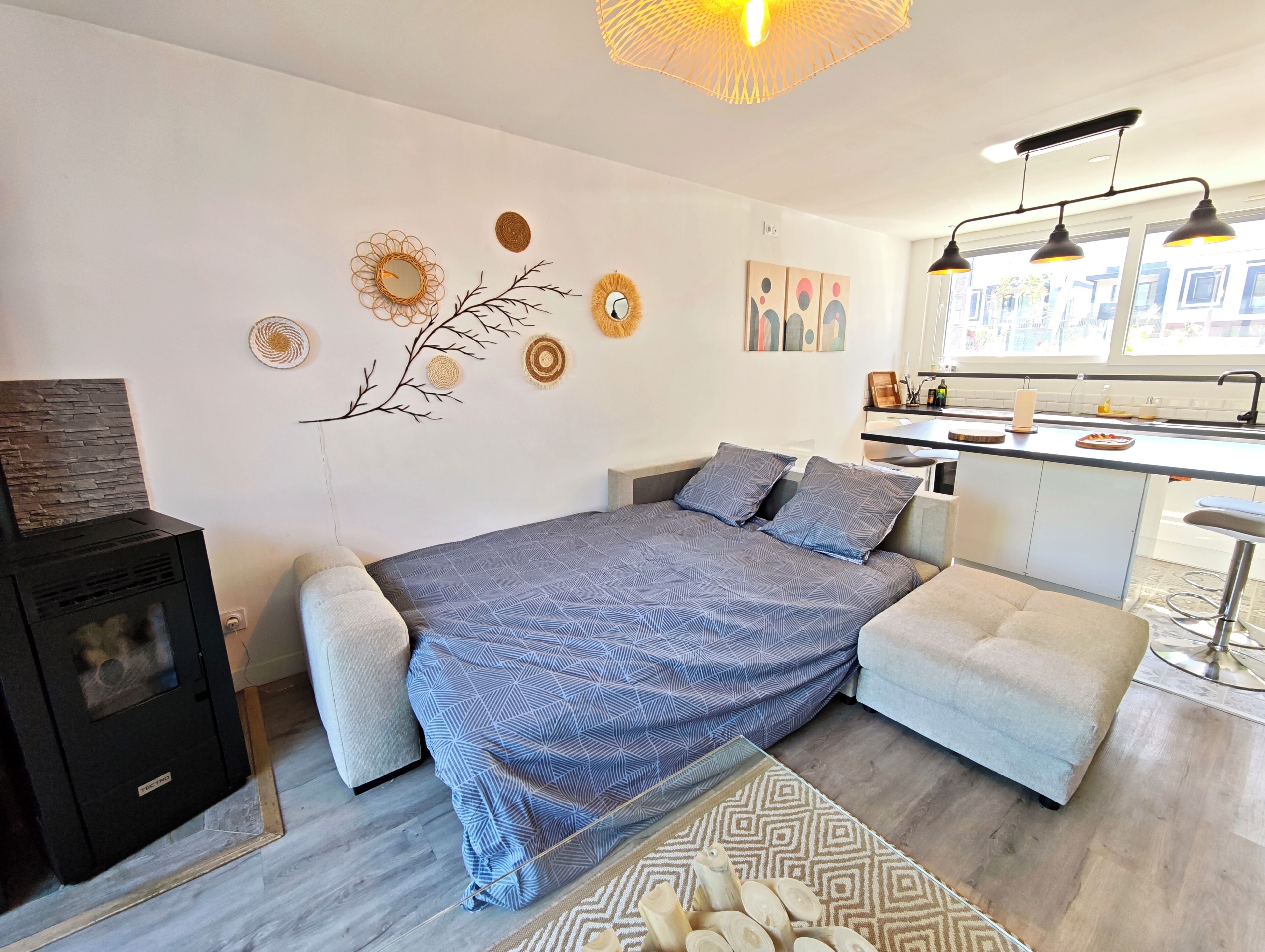 A modern bedroom with a bed, a small sofa, a kitchen area, and a fireplace.