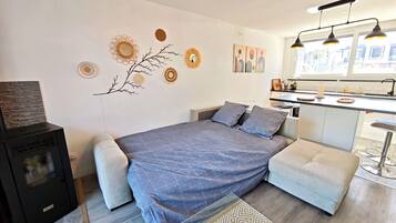 A modern bedroom with a bed, a small sofa, a kitchen area, and a fireplace.