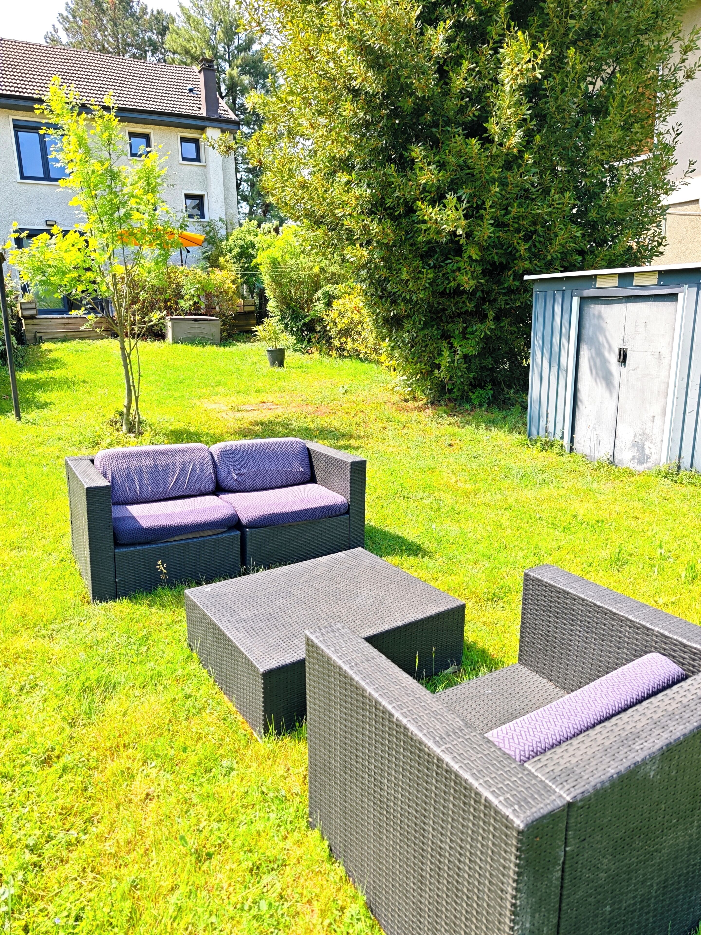 Un jardin avec des meubles d’extérieur, un abri de jardin et une maison en arrière-plan.