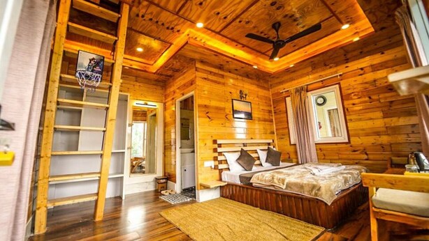 Camera da letto in una baita di legno, con un letto, una ventola a soffitto, una finestra con tende e una porta che dà su un'altra stanza.