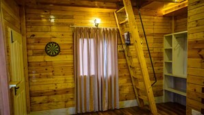 Una stanza con pareti in legno, un bersaglio da freccette, una scala e una finestra con tende.