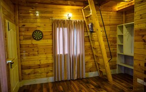 Una habitación con paredes de madera, un dardo, una escalera y una ventana con cortinas.