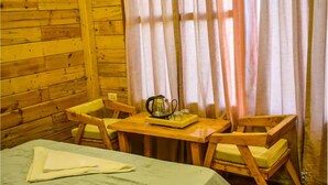 Una camera in baita di legno con un letto, due sedie di legno, un tavolino con un bollitore e una finestra con tende.