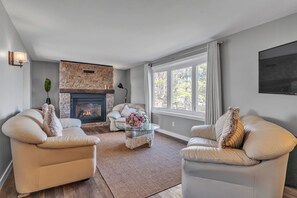 Ein Wohnzimmer mit zwei Sofas, einem Kamin, einem Couchtisch mit Blumen und großen Fenstern.